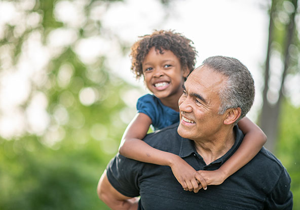 A dad outside with his young daughter on his back
